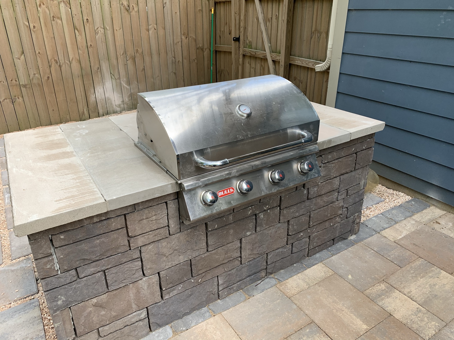 Built-in stainless grill set in a stacked-stone base with a stone countertop, on a paver pad