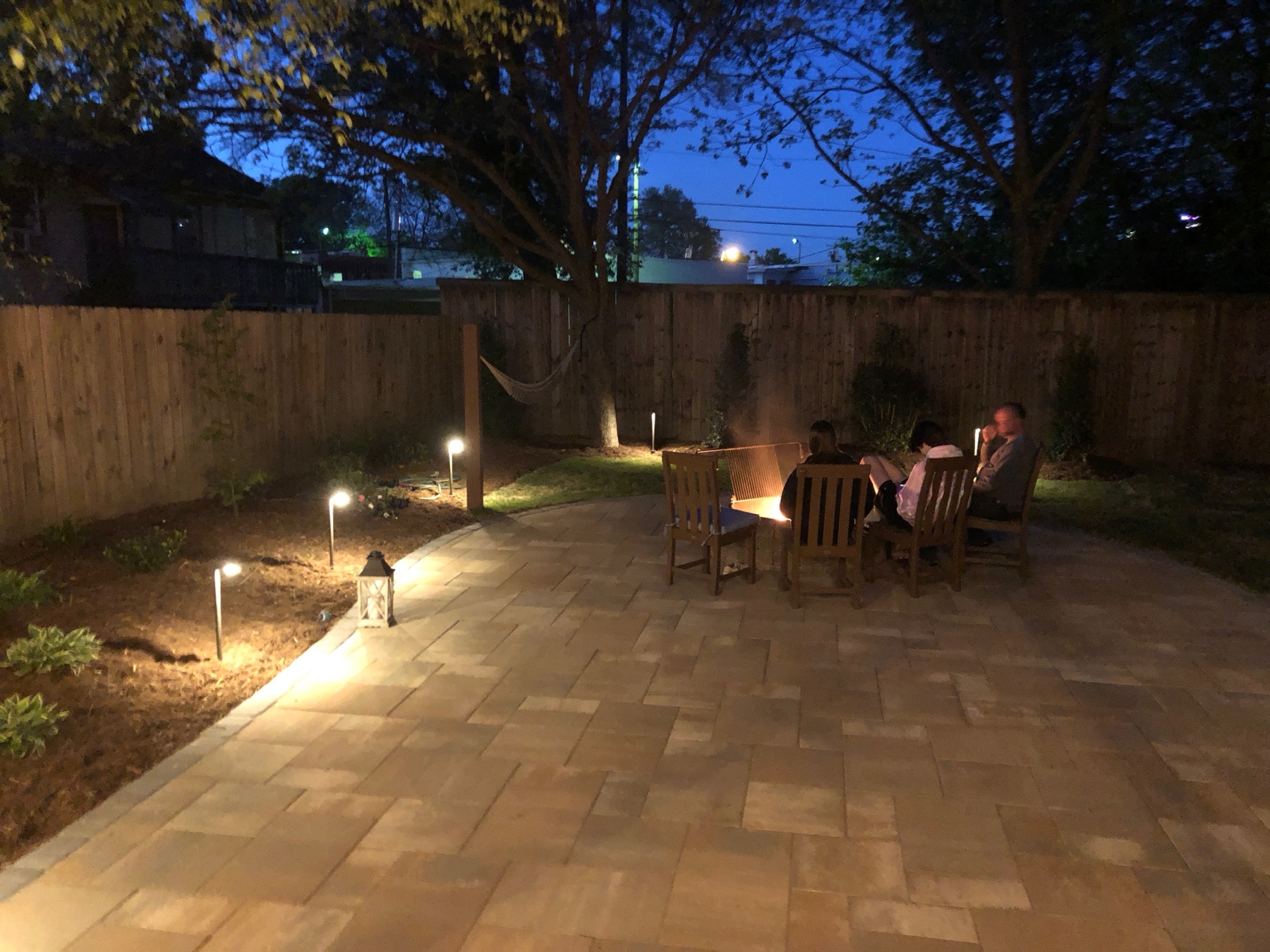 The patio at dusk with path lights glowing along the planting beds and the fire pit lit