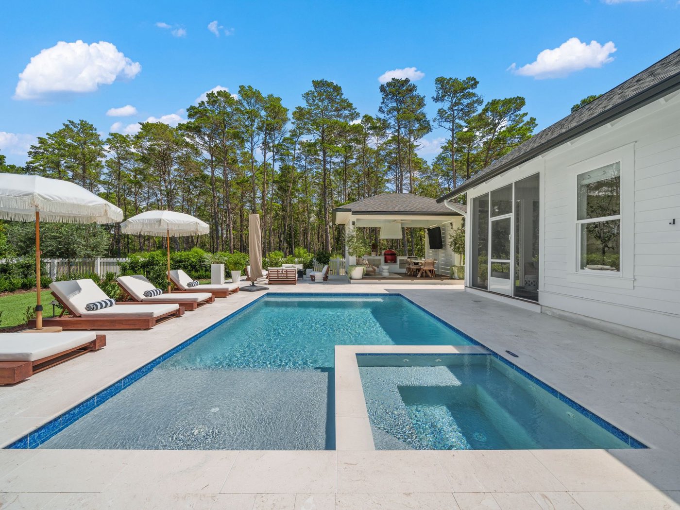 Pool and spa on a pale stone paver deck with lounge chairs and a covered cabana