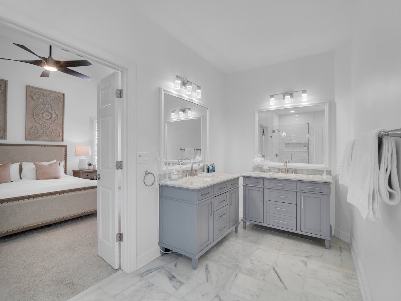 After: Two gray vanities with marble tops and white framed mirrors, open door to the bedroom, marble floor