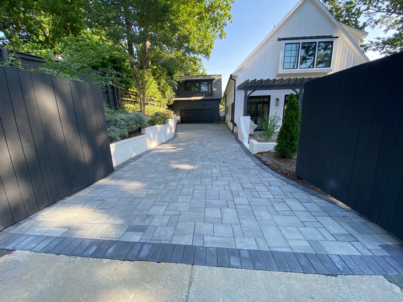 After: Gray paver driveway with a dark border between black wood fences, leading to a detached garage