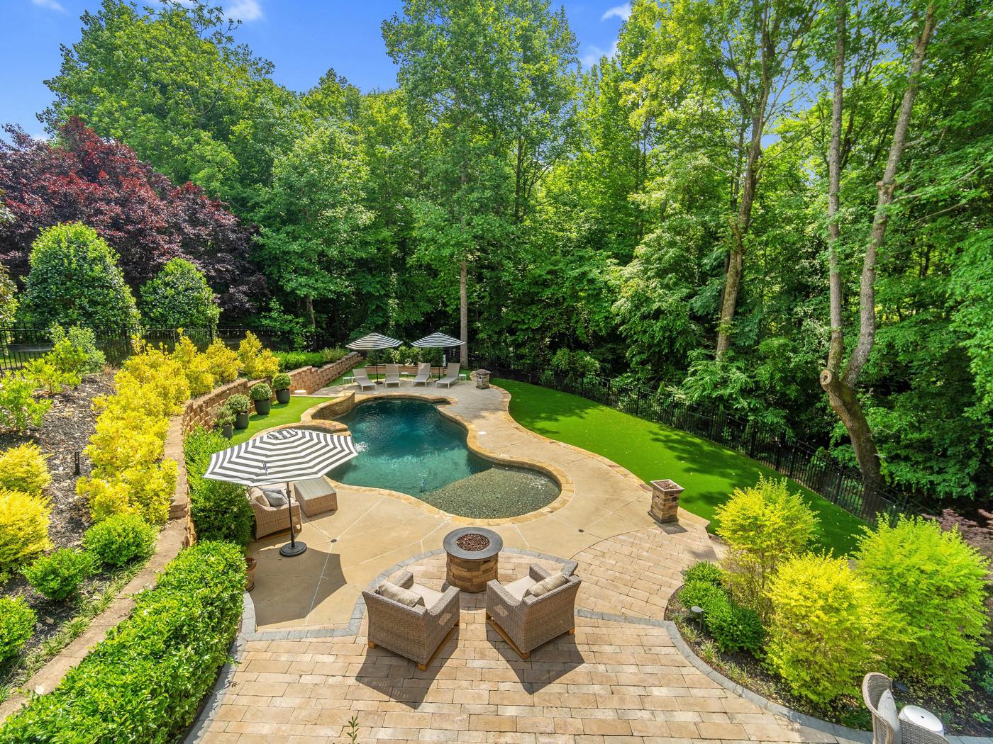 After: Backyard with a paver patio, fire pit, pool, turf lawn and layered planting