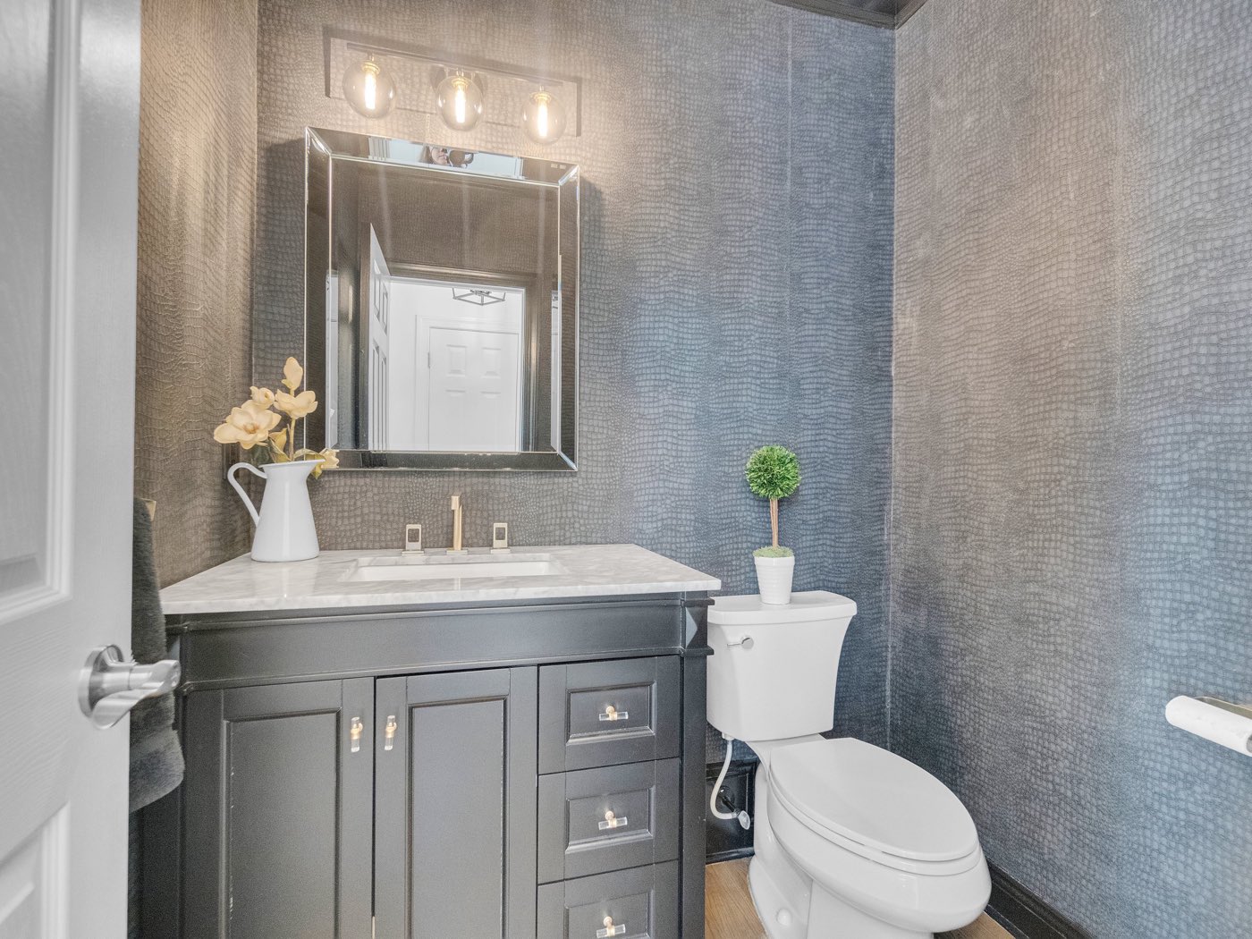 After: Dark vanity with marble top and beveled mirror against textured blue-gray wallpaper
